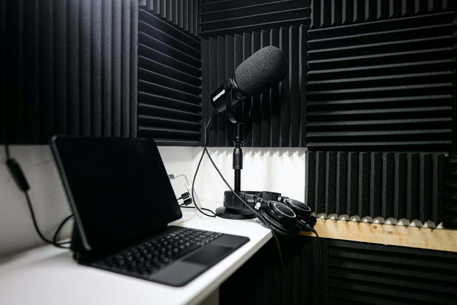 A laptop sitting on top of a white-desk beside a black mic and headphones